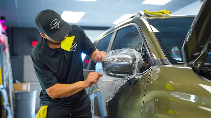 Technician applying clear paint protection film to a vehicle hood